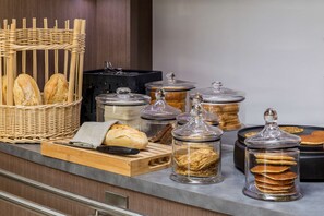 Mostrador de buffet con diversos alimentos, como pan, bollería y frascos con conservas.