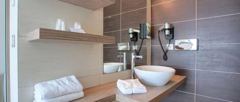 Un baño moderno con tocador de madera, un lavamanos grande de color blanco y un espejo encima.