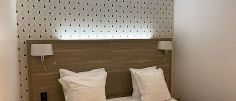 A neatly made bed with two pillows, a wooden headboard, and wall-mounted lamps.