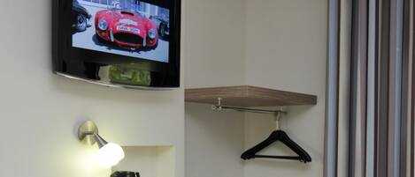 A compact room with a desk, chair, TV, and a hanging coat rack.