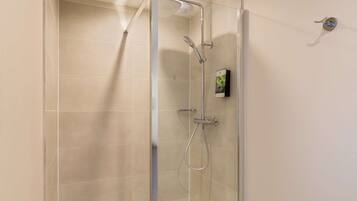 Ducha con mampara de vidrio, cabezal de ducha de mano y grifo empotrado.