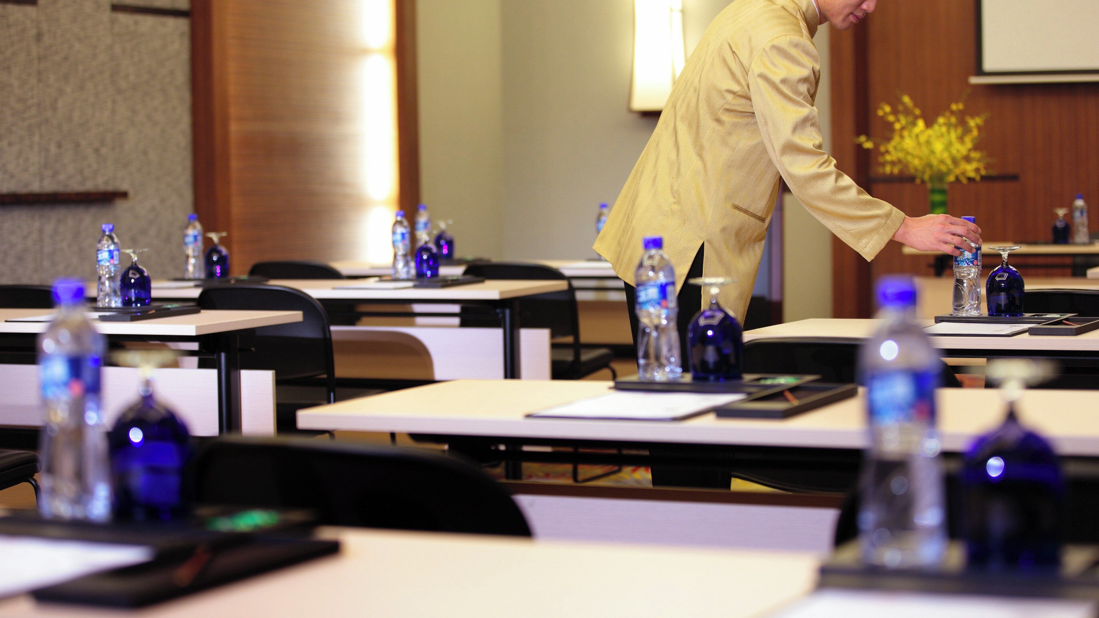 A conference room with tables set up for a meeting, each with a bottle of water and a glass.