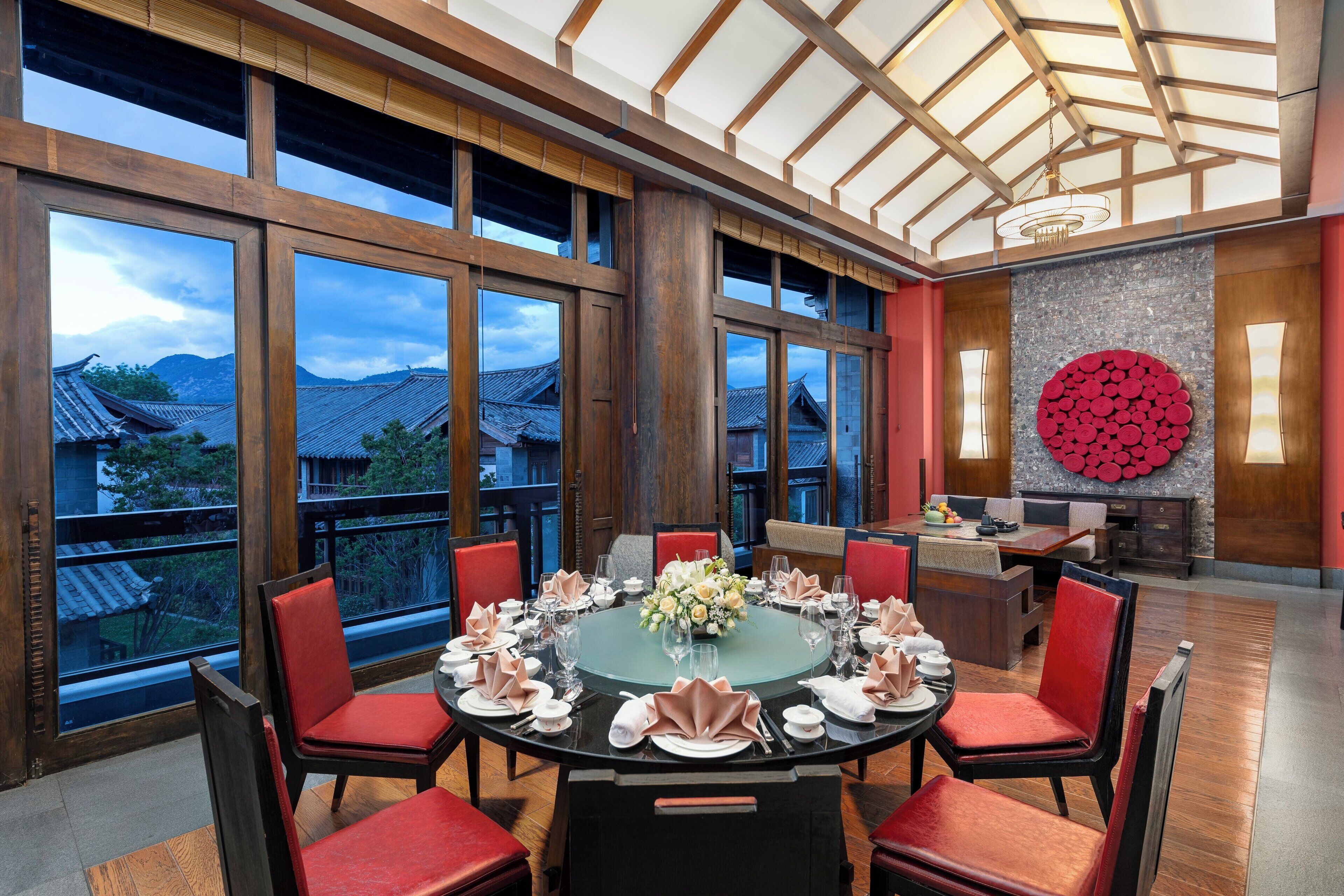Comedor con una mesa redonda dispuesta para seis personas, rodeada de sillas rojas, y vistas a edificios tradicionales.