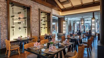 A restaurant with wooden tables and wicker chairs, large windows, and hanging light fixtures.