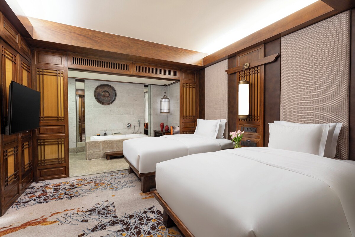A hotel room with two beds, a television, a bathroom with a bathtub, and a shower.