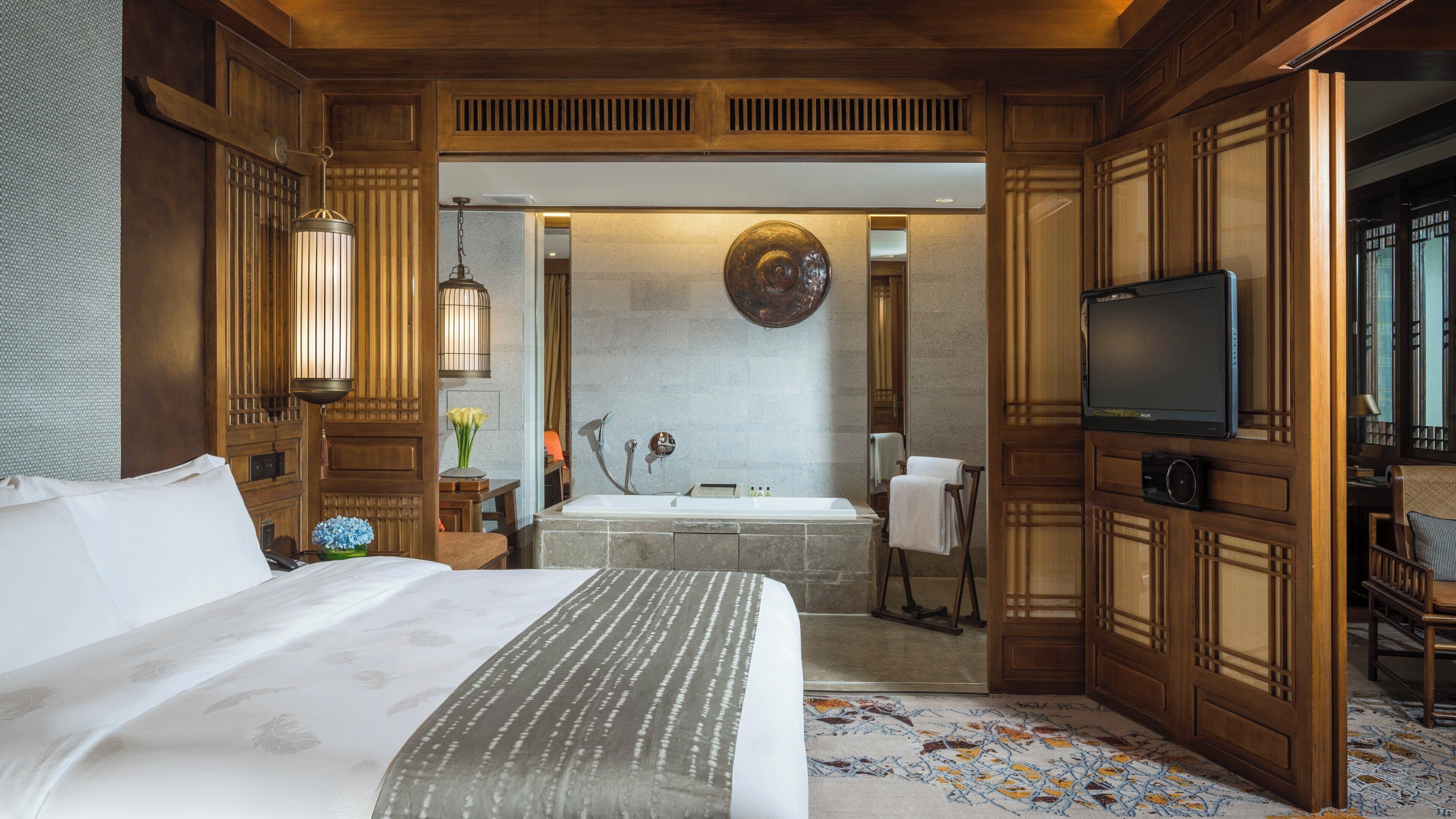 A hotel room with a large bed, a television, a bathroom with a bathtub, and wooden paneling.