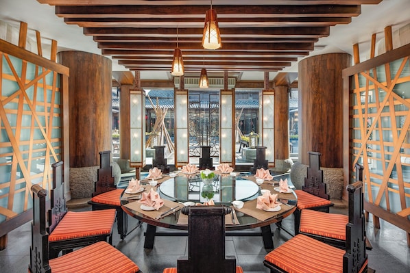Un comedor de estilo tradicional con mesas redondas, sillas de madera y una mesa de vidrio central.
