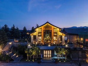 A traditional-style building with a large entrance, a staircase leading up to it, and a well-lit outdoor area with palm trees. - InterContinental Lijiang Ancient Town Resort by IHG (Lijiang)