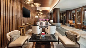 Un lobby moderno con un panel de madera, un televisor de pantalla plana, una mesa de centro de mármol y dos sillones.