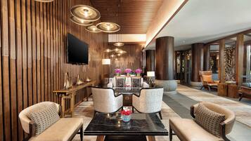 Un lobby moderno con un panel de madera, un televisor de pantalla plana, una mesa de centro de mármol y dos sillones.