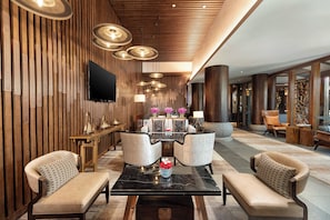 Un lobby moderno con un panel de madera, un televisor de pantalla plana, una mesa de centro de mármol y dos sillones.