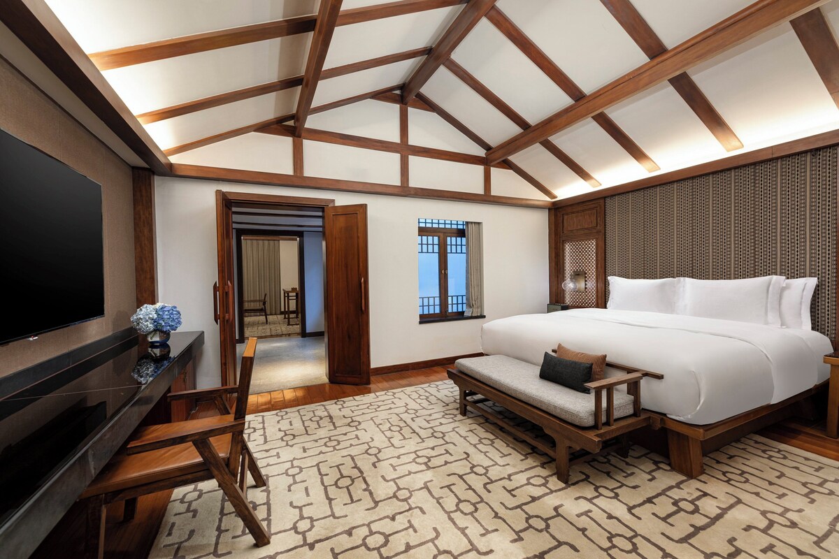 A modern bedroom with a large bed, a TV, and a wooden ceiling structure.