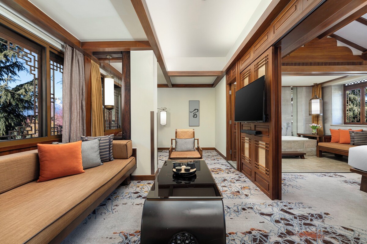 A hotel room with a wooden sofa, a coffee table, a TV, and a bed.