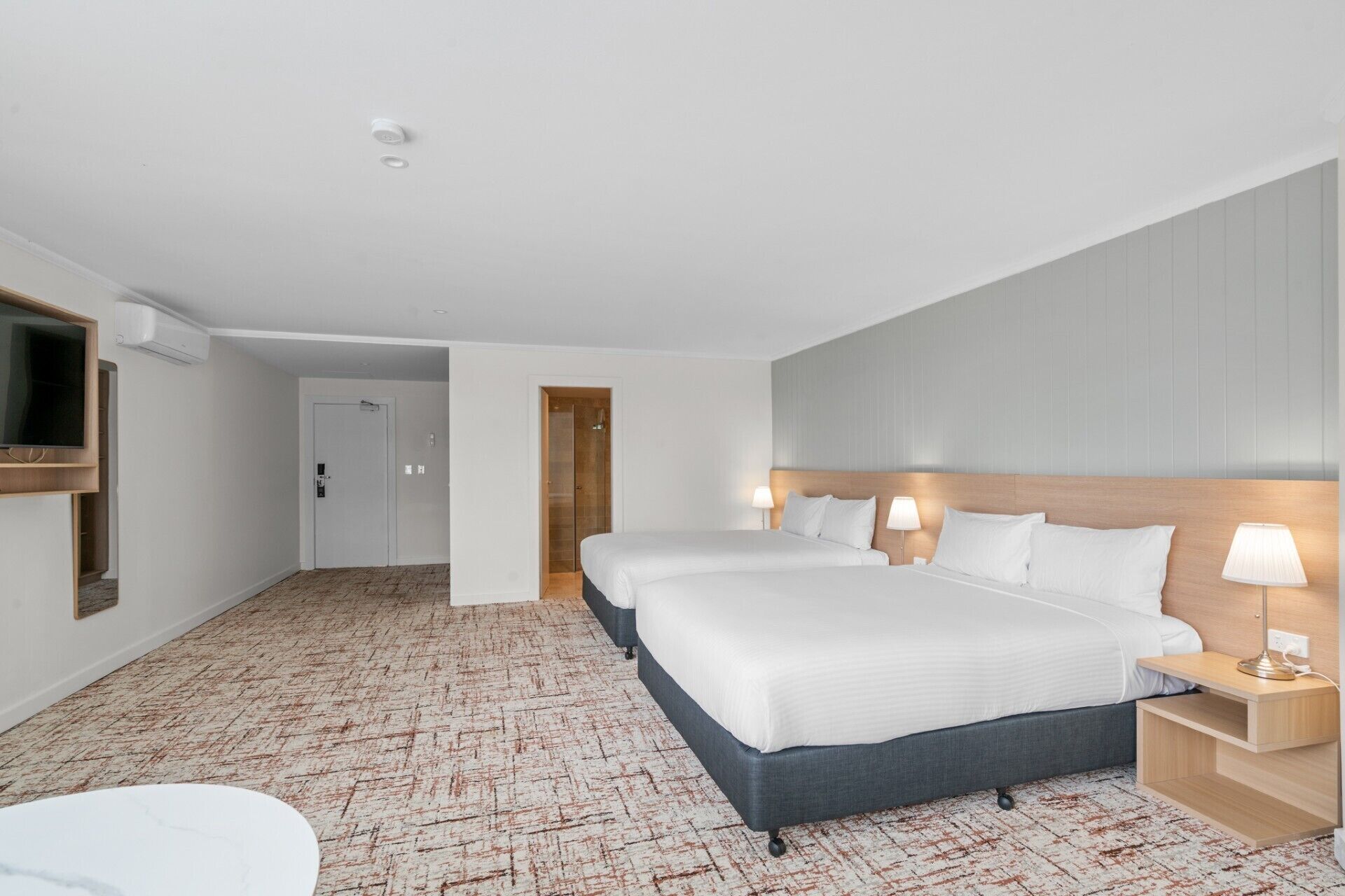 A hotel room with a large bed, two bedside tables with lamps, a TV mounted on the wall, and a door leading to another room.