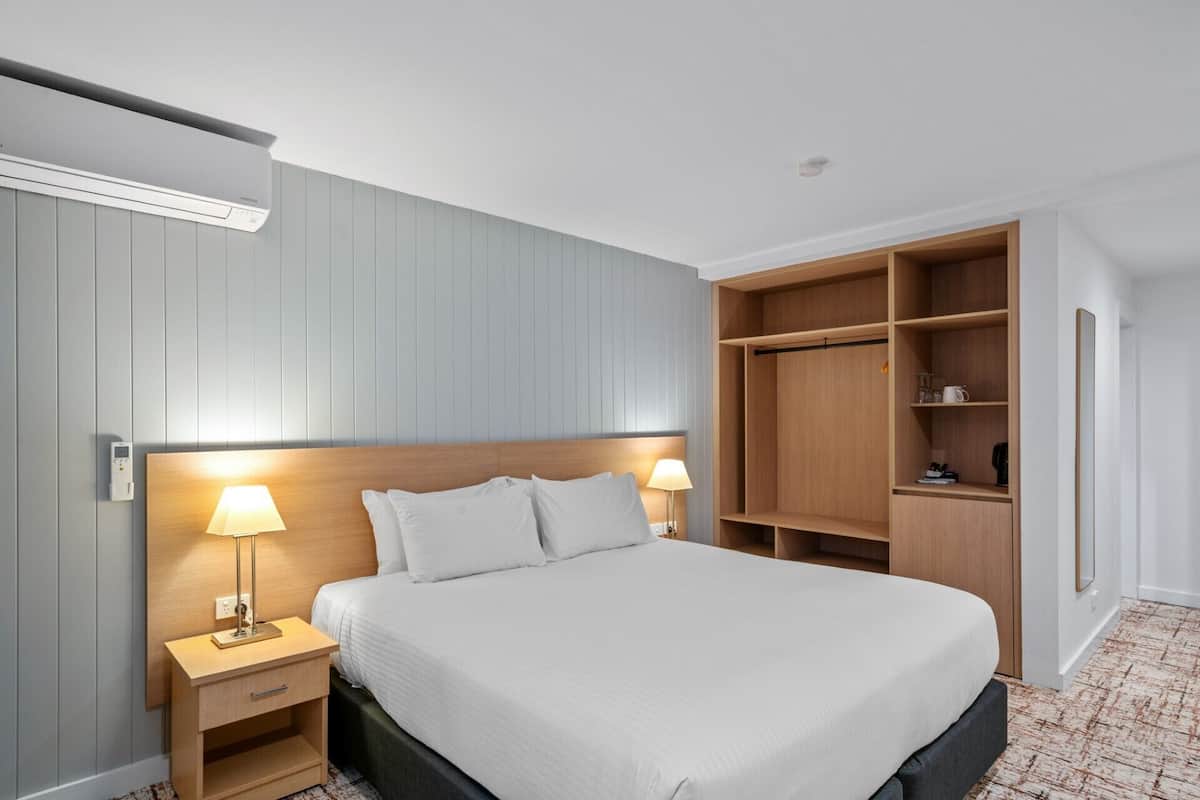 A hotel room with a bed, bedside lamps, a nightstand, a wardrobe, and a mirror.