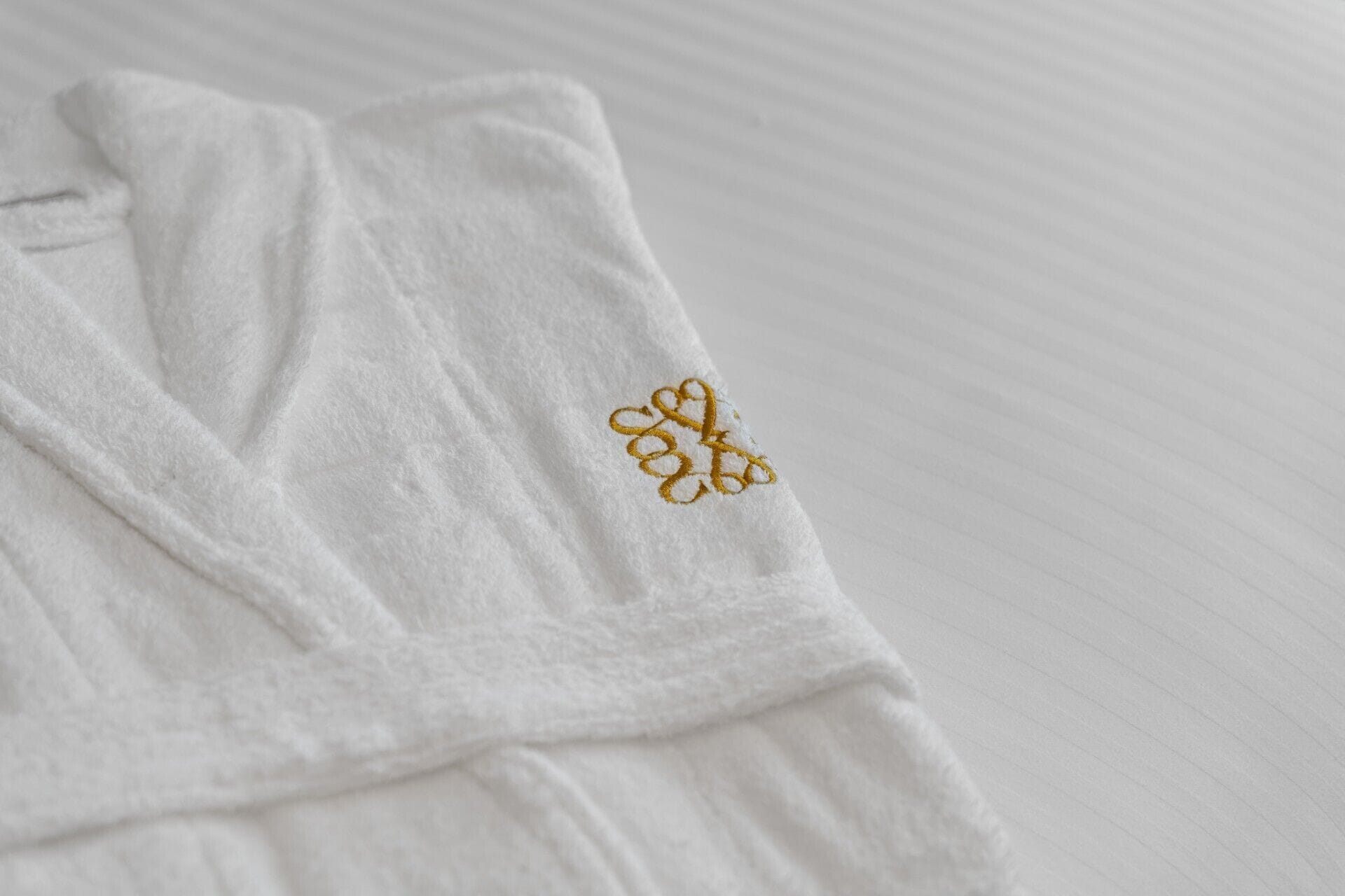 Toalha branca com desenho dourado bordado em superfície texturizada.