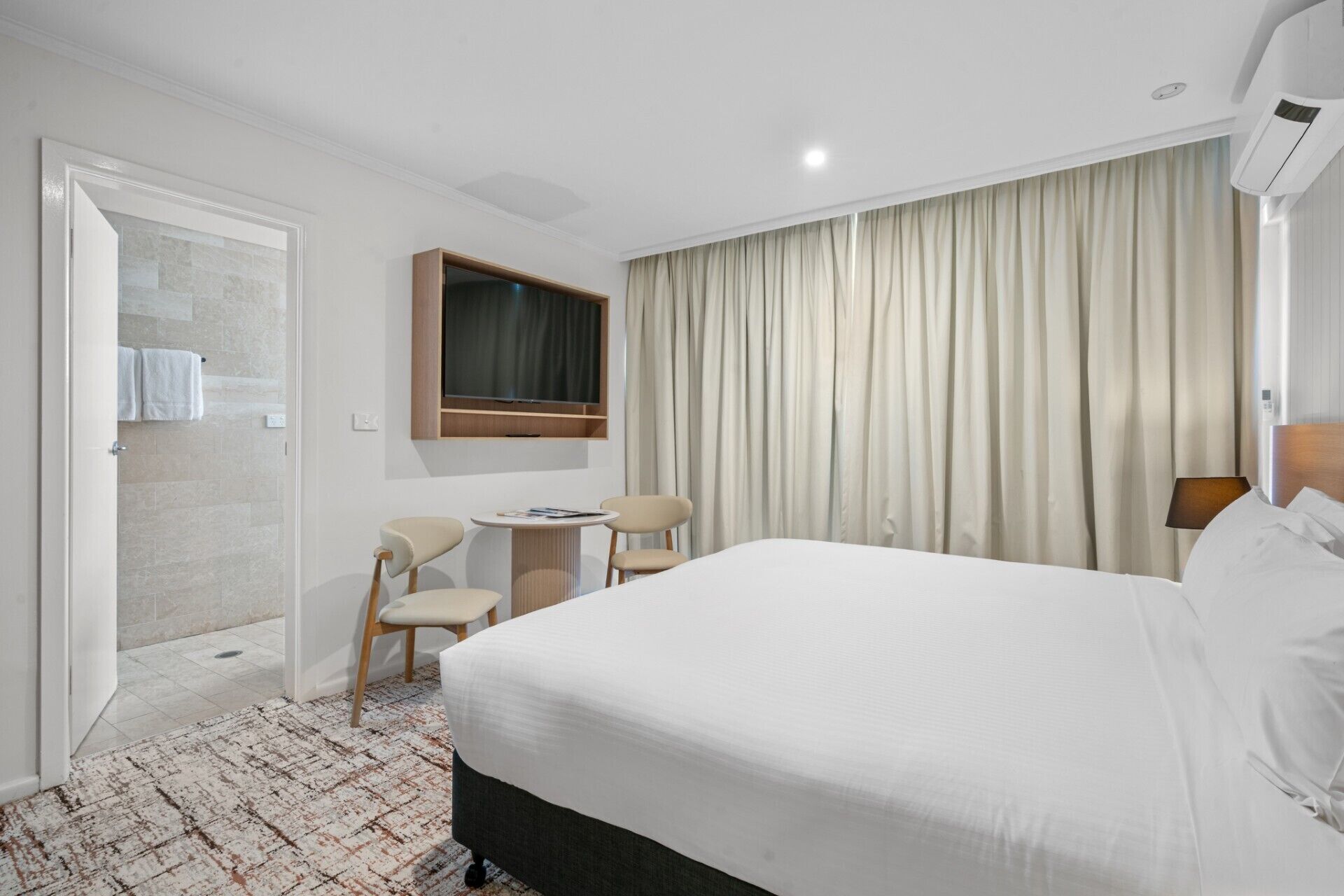 Ein Hotelzimmer mit einem großen Bett, einem Schreibtisch, zwei Stühlen, einem Fernseher und einem Badezimmer mit Dusche und WC.