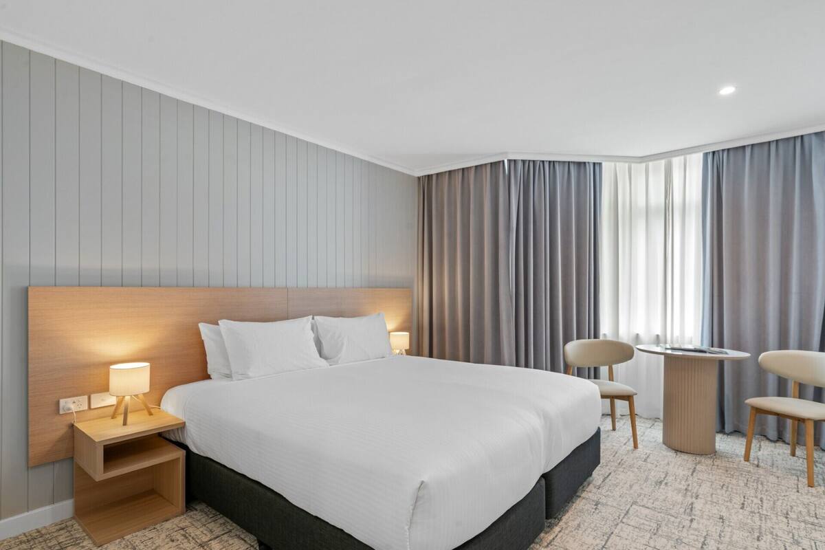 A hotel room with a large bed, bedside tables, a desk, and chairs.