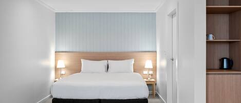 Habitación de hotel moderna con una cama grande, dos lámparas de noche, un cabecero de madera y una estantería empotrada con una tetera.