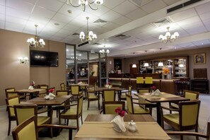 A restaurant with multiple tables and chairs, a bar area, and a television mounted on the wall.