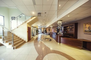 A spacious lobby with a grand staircase, a reception desk, and a large painting on the wall.