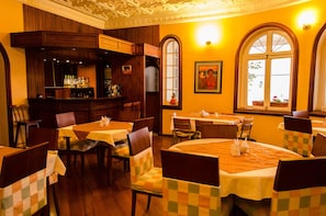 A restaurant with multiple tables, wooden chairs, and a bar area with bottles. - Hotel La Casona (Cuenca)