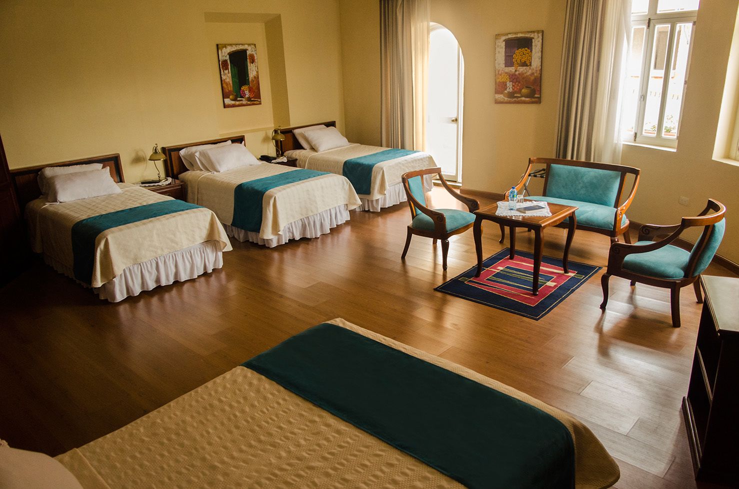 Una camera d'albergo con due letti singoli, un tavolino con sedie e una grande finestra.