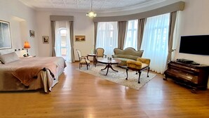 A hotel room with a bed, a sofa, a chair, a small table, a television, and a piano. - Hotel La Casona (Cuenca)