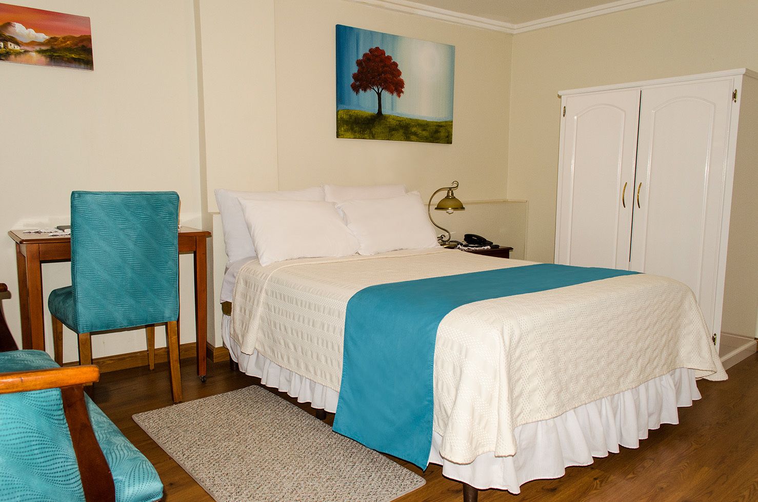 A bedroom with a bed, a chair, a desk, a lamp, and a wardrobe.