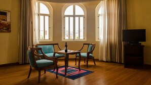 A room with a wooden floor, two chairs, a table, a television, and three windows with curtains. - Hotel La Casona (Cuenca)