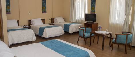 A hotel room with three beds, a television, a small table with a water bottle, and two chairs.