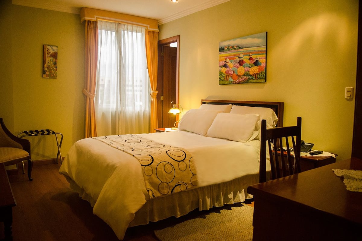 Une chambre d’hôtel avec un lit, un bureau, une chaise, une lampe et un tableau au mur.