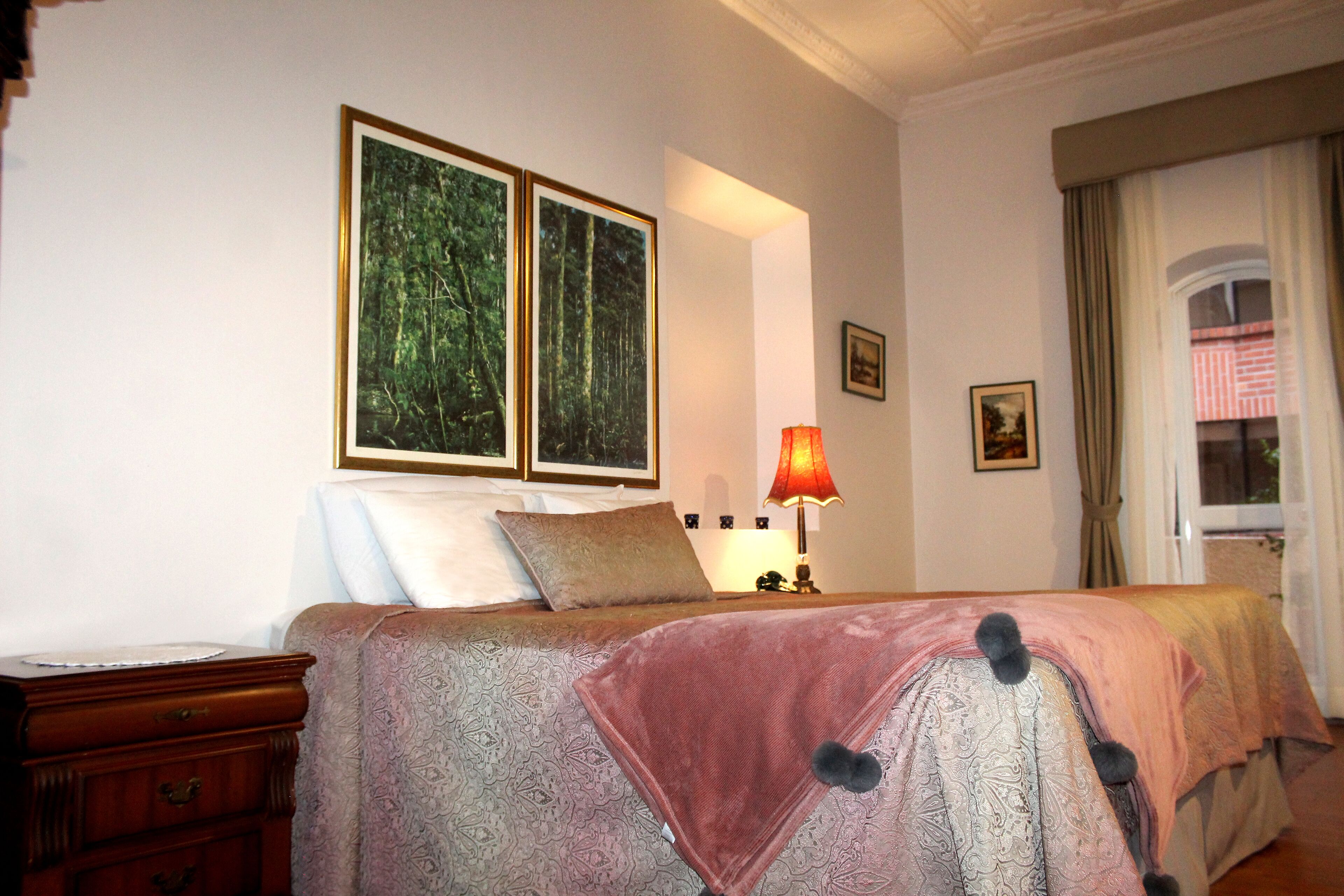 A hotel room with a bed, a nightstand, a lamp, and two framed pictures on the wall.