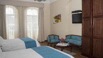 A hotel room with two beds, a television, a wooden wardrobe, and a small table with a vase of flowers.