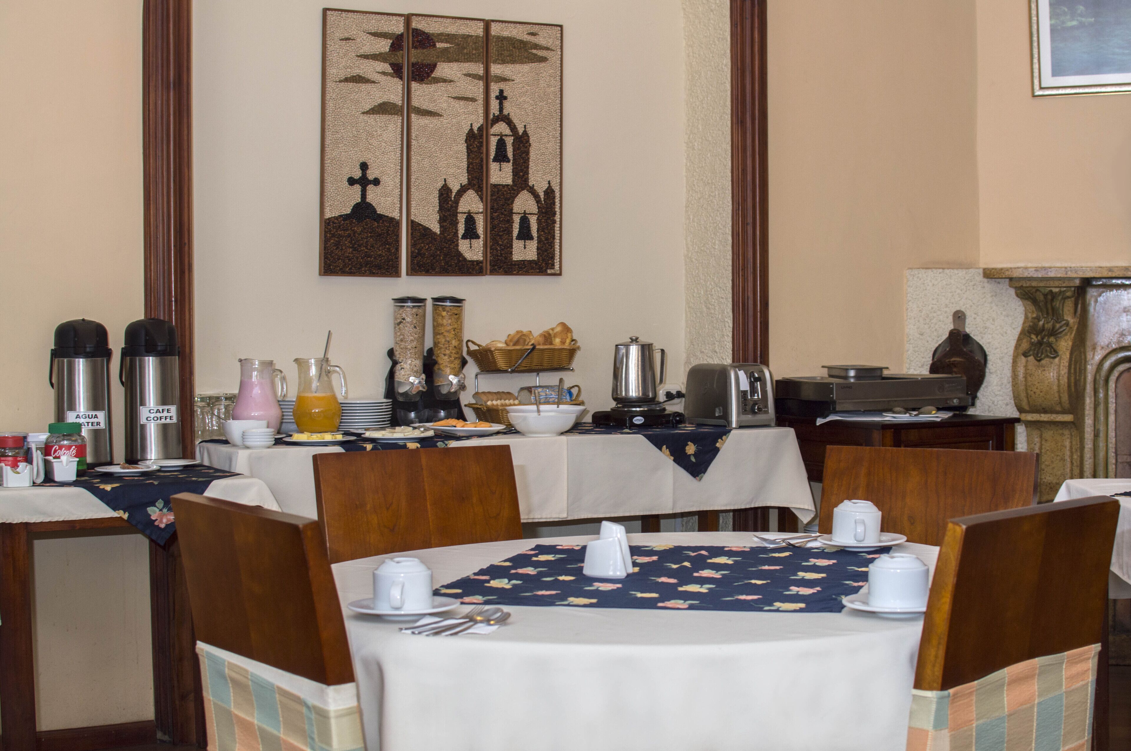 A dining area with tables set for breakfast, including coffee makers, a fruit bowl, and a basket of bread.