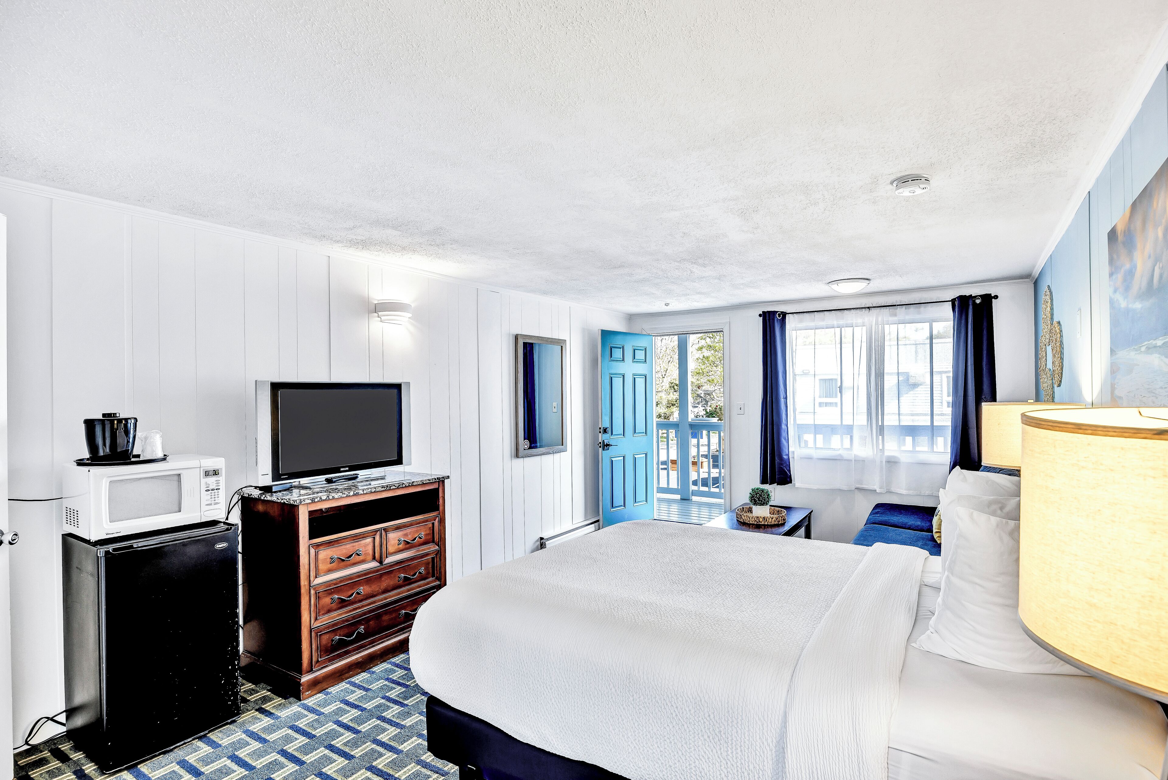 A hotel room with a bed, a television, a microwave, a dresser, and a window with curtains.
