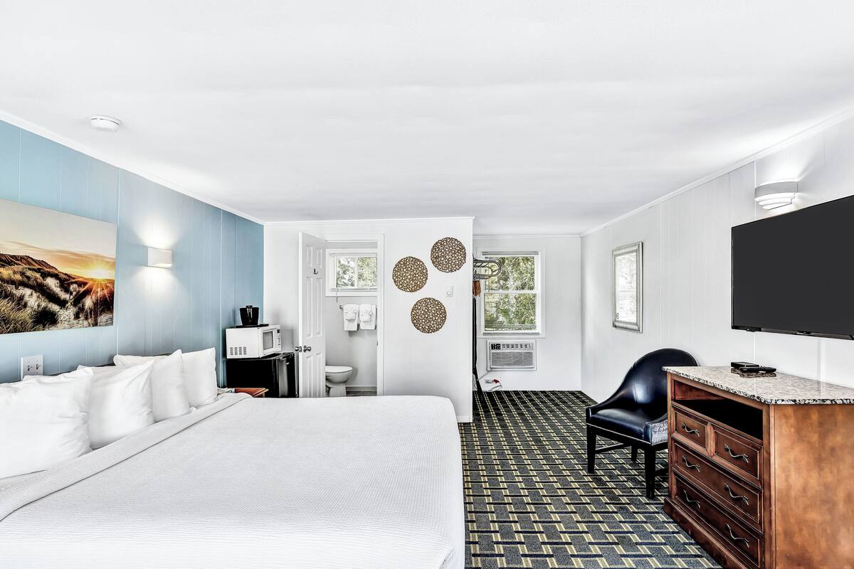Une chambre d’hôtel avec un grand lit, un bureau doté d’un téléviseur à écran plat, une chaise et une commode.