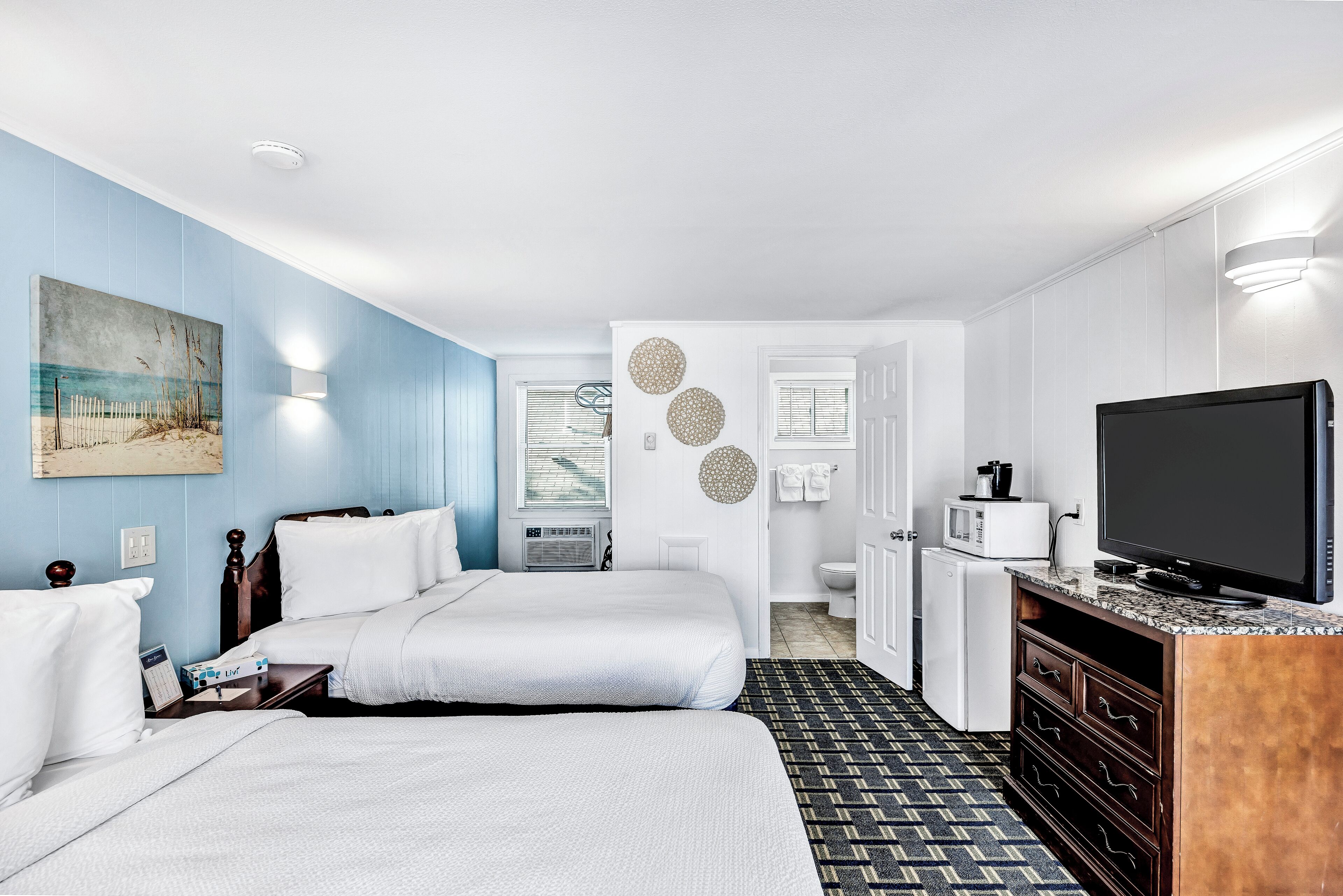 A hotel room with two beds, a TV, a microwave, and a small kitchenette.