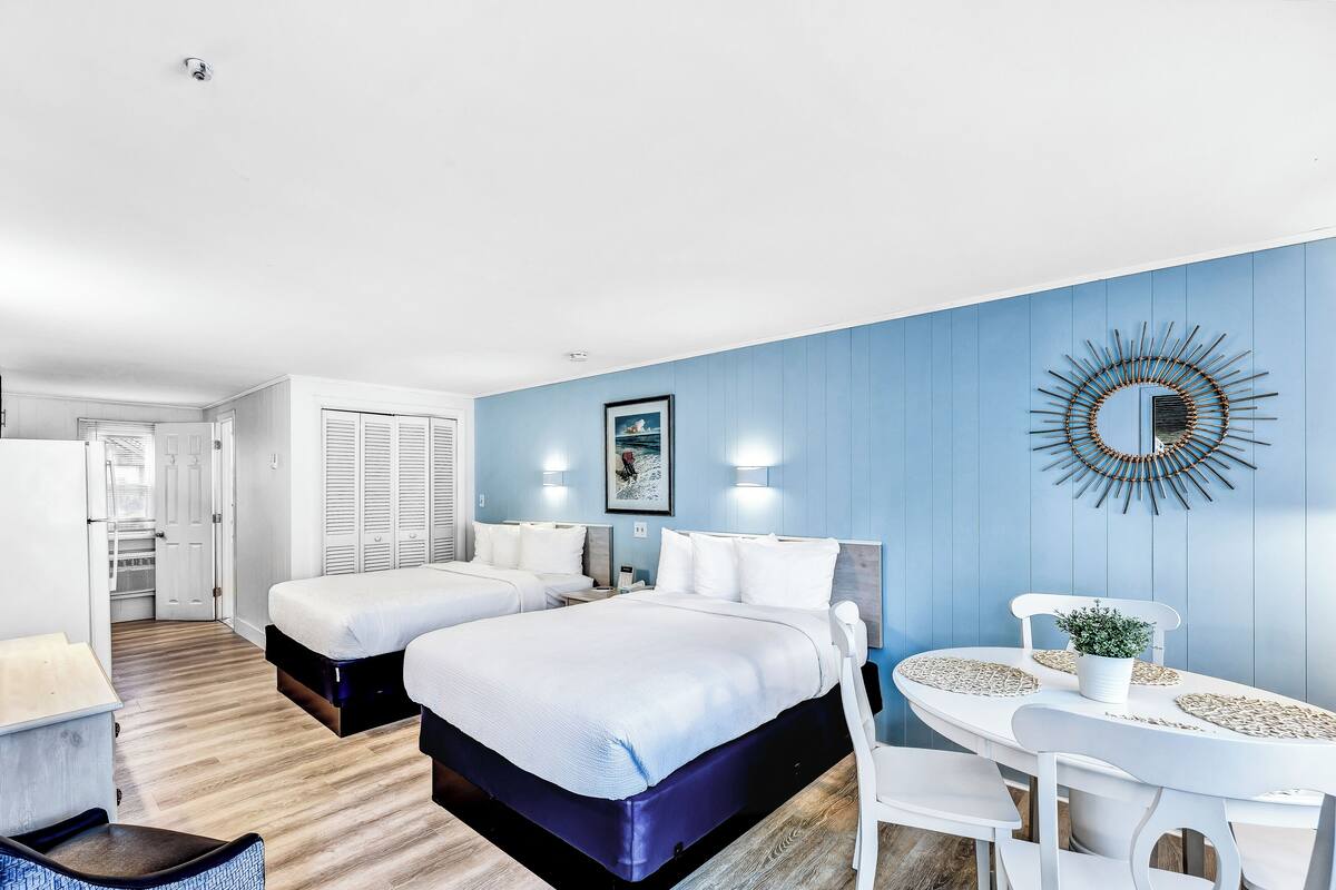 Une chambre d’hôtel avec deux lits, un coin repas comprenant une table et des chaises, et un miroir fixé au mur.