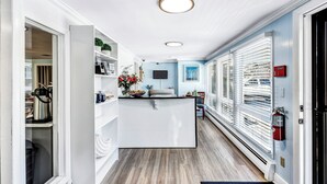 Un couloir étroit avec un coin cuisine comprenant un plan de travail blanc, un évier et une fenêtre avec des stores.
