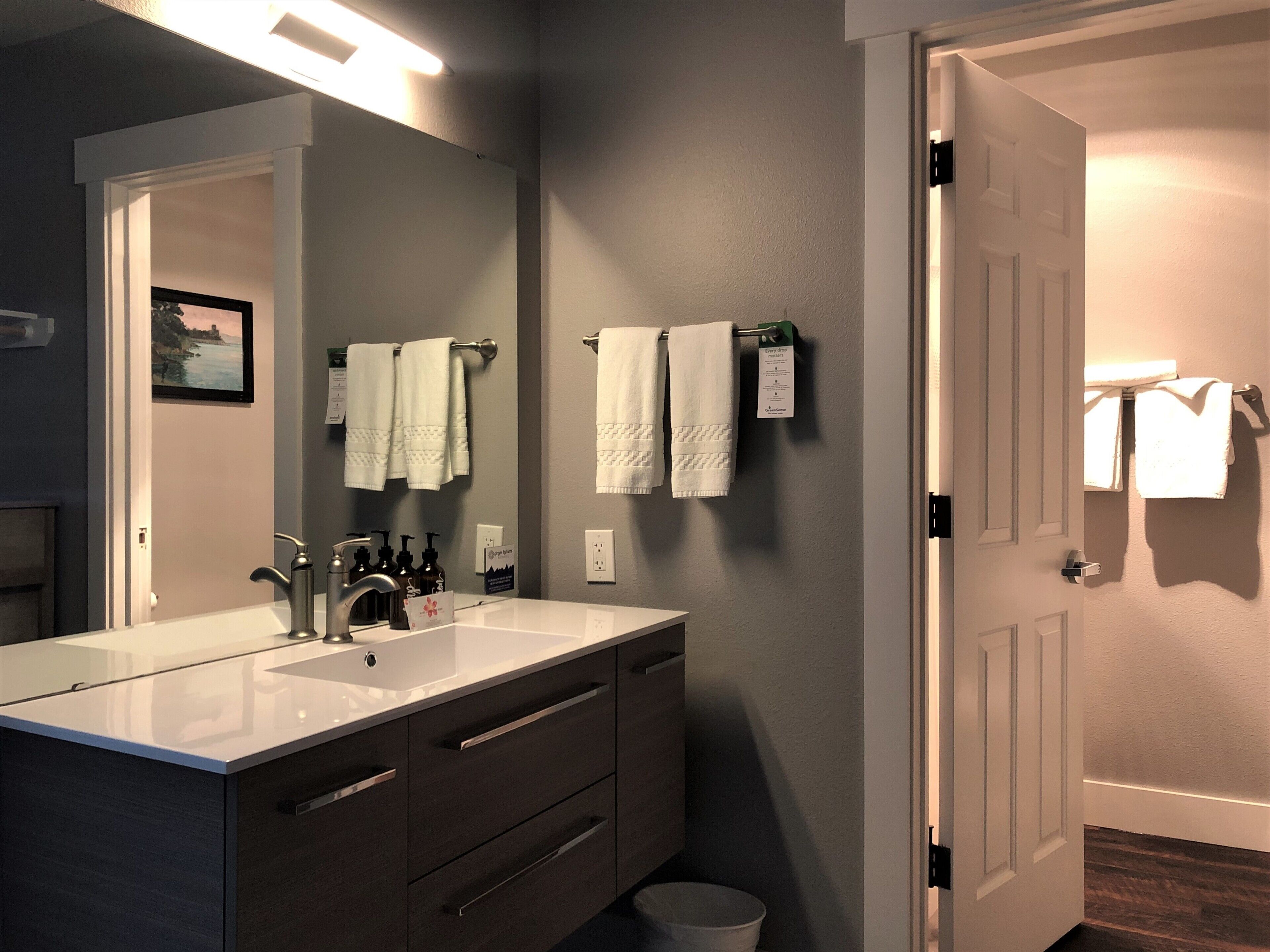 A bathroom with a double sink, a mirror, and two towels hanging on the wall.