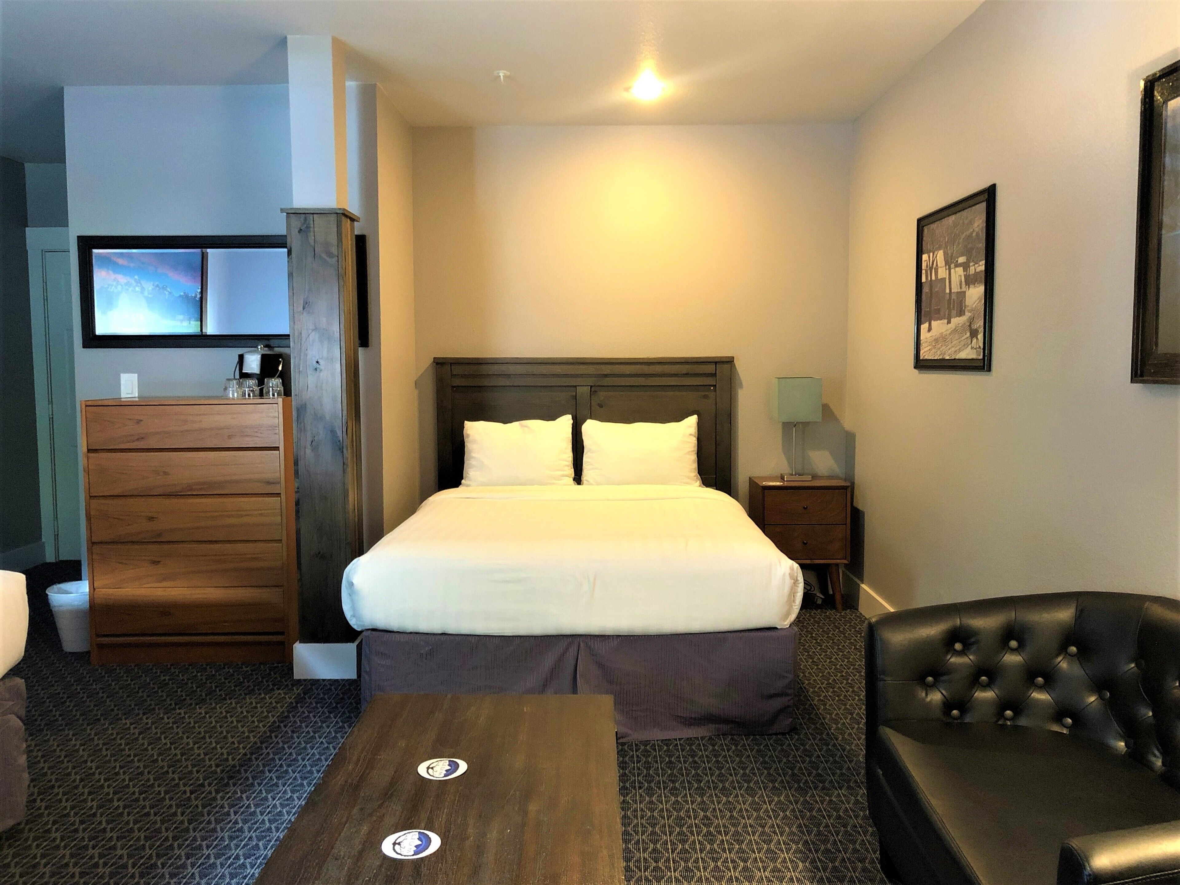 Une chambre d’hôtel avec un lit, une commode en bois, un bureau, une chaise et un téléviseur fixé au mur.