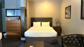 Une chambre d’hôtel avec un lit, une commode en bois, un bureau, une chaise et un téléviseur fixé au mur.