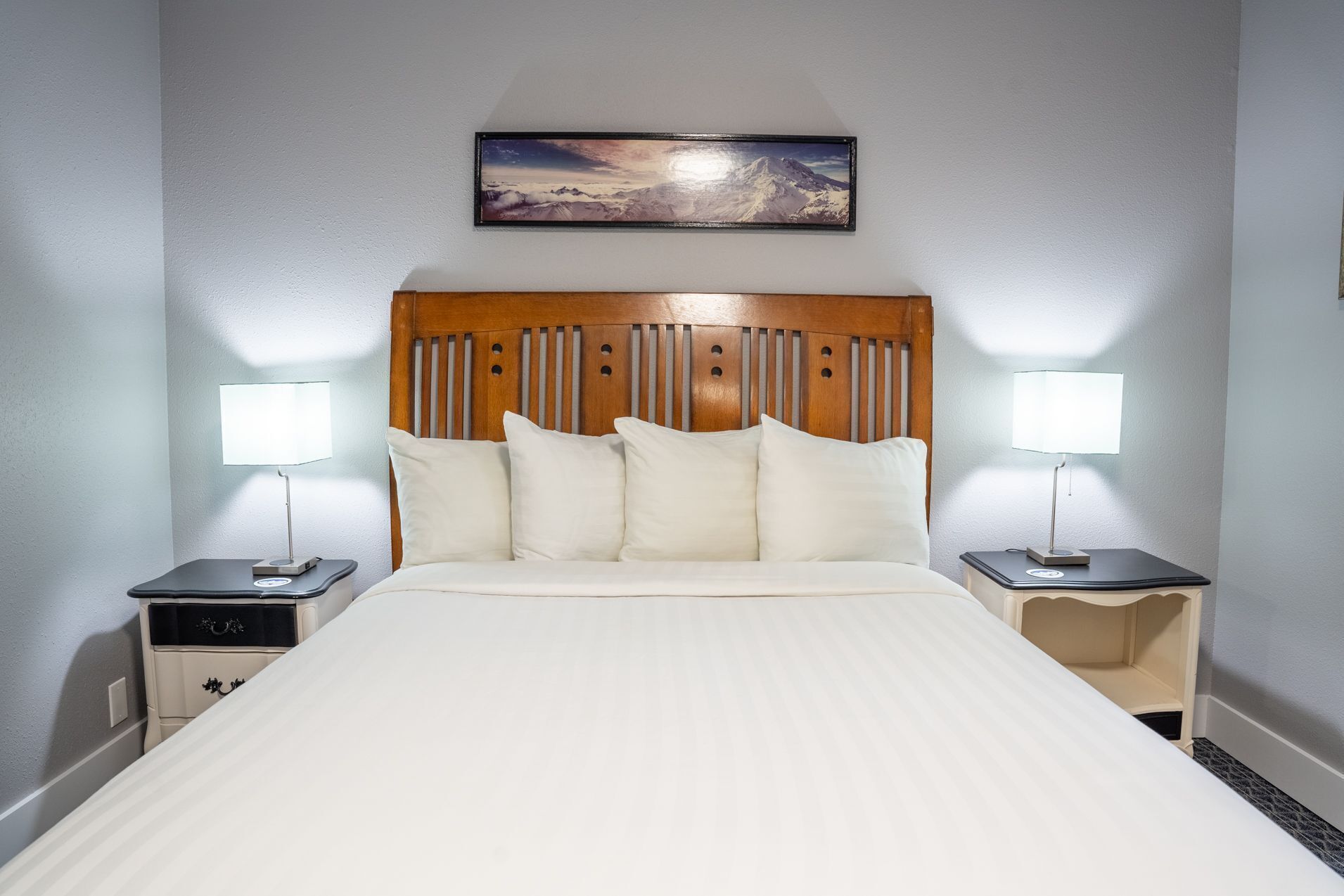 A hotel room with a large bed, two bedside tables with lamps, a wooden headboard, and a framed picture on the wall.