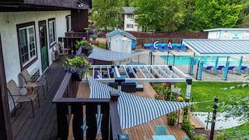 Relax on the deck surrounded by lush greenery and a swimming pool, with comfortable seating and lounge chairs.