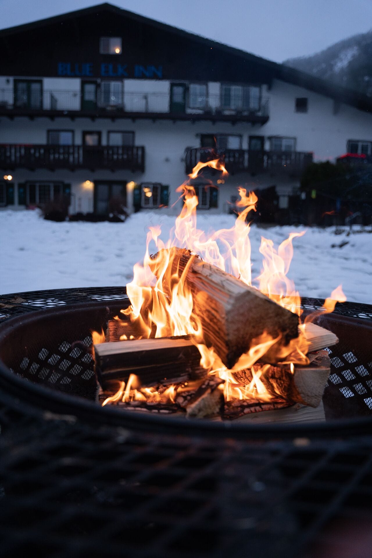 Ein Feuerkorb mit brennenden Holzscheiten vor einem Gebäude mit Balkonen und einem Schild mit der Aufschrift "BLUE ELK INN".