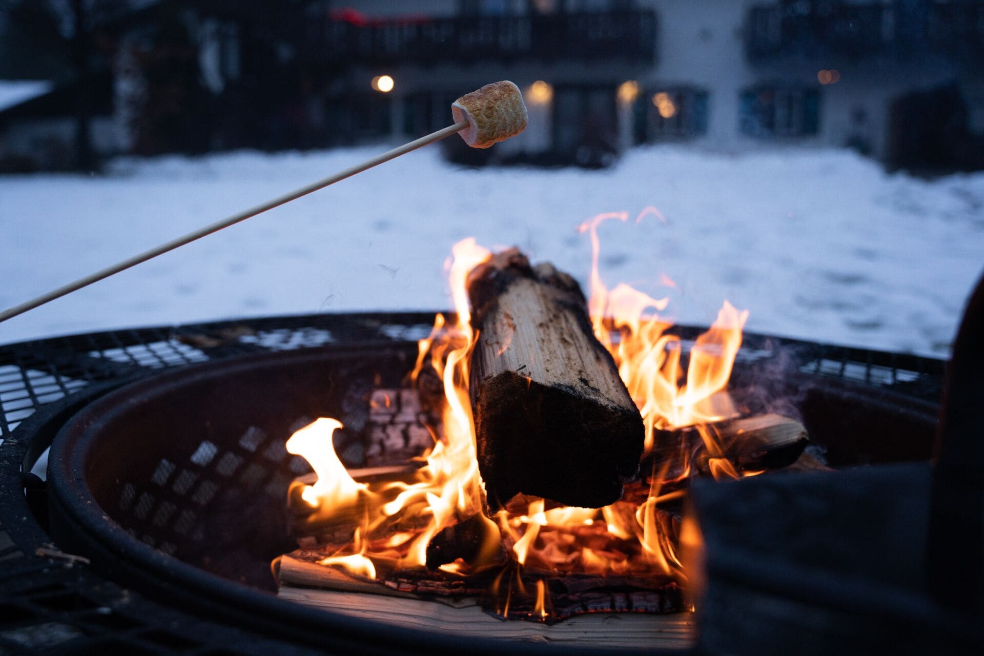 A campfire with a marshmallow on a stick, surrounded by logs and flames.