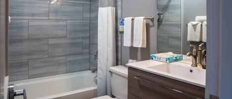 Un baño con bañera, inodoro, tocador con espejo y cortina de ducha.