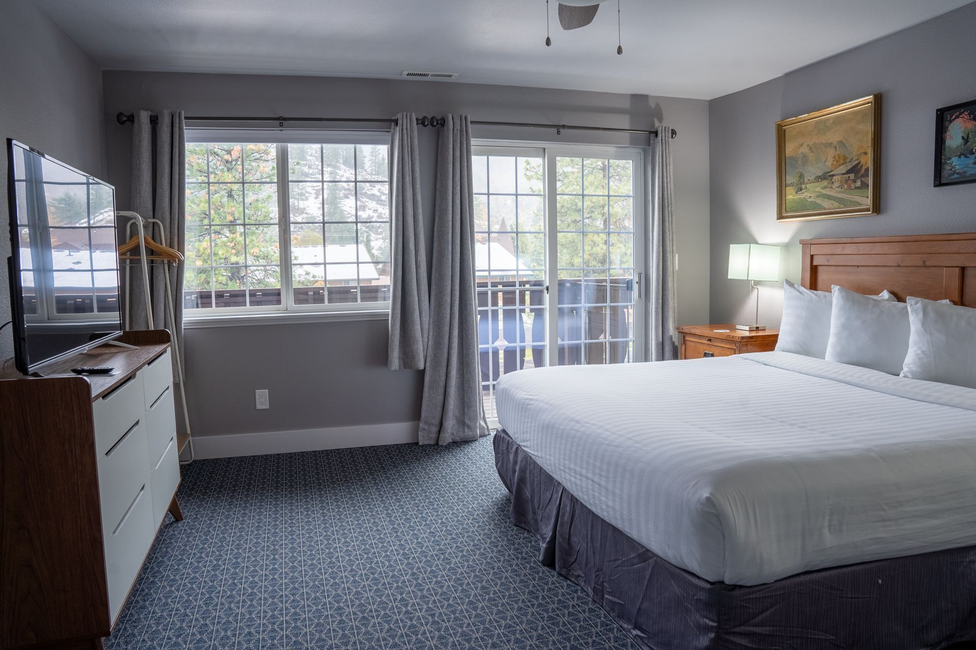 Une chambre d’hôtel comprenant un lit, un bureau avec une chaise, une télévision et une fenêtre avec des rideaux.