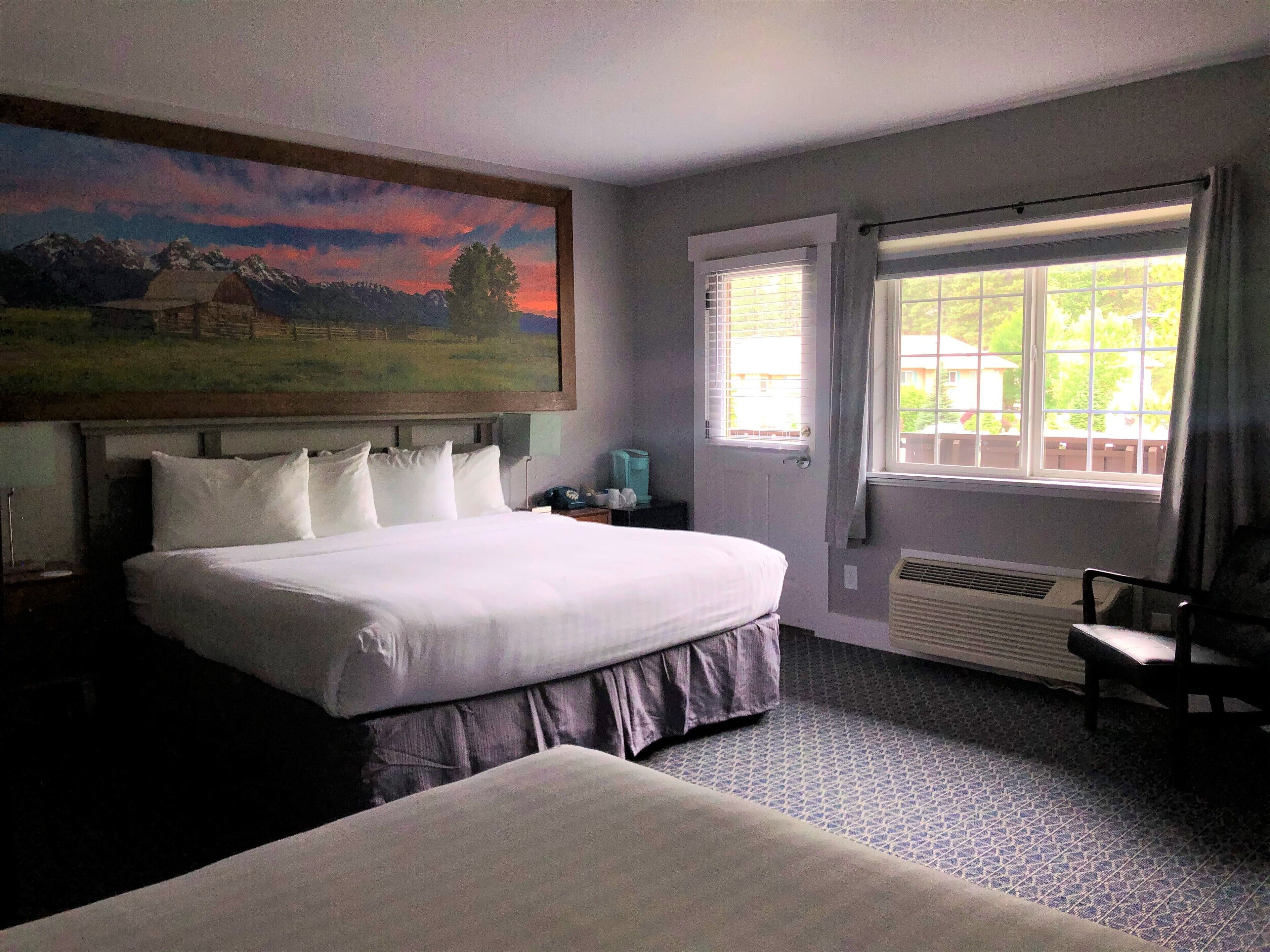 Habitación de hotel con una cama grande, un cuadro de un paisaje, una ventana con cortinas y un radiador.